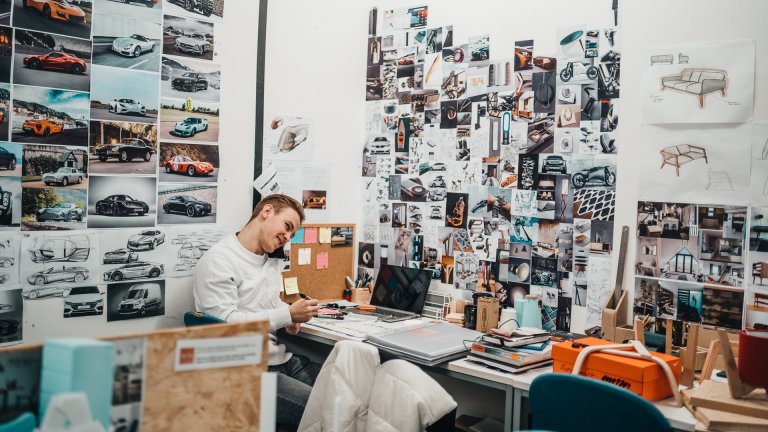 Ein Designer sitzt an seinem Schreibtisch und blickt auf eine Wand voll Skizzen.