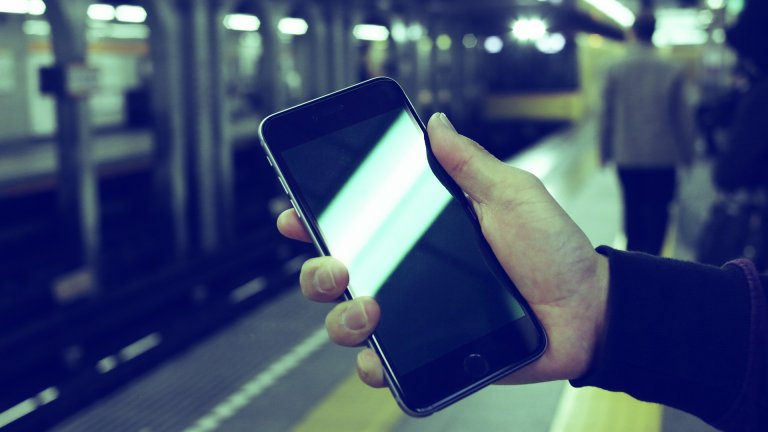 Hand mit Mobiltelefon am Bahnsteig