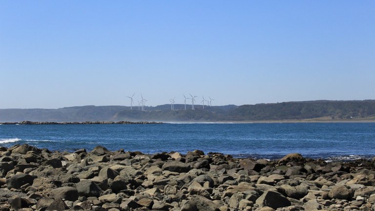 Windräder am Horizont hinter Wasser und Steinufer