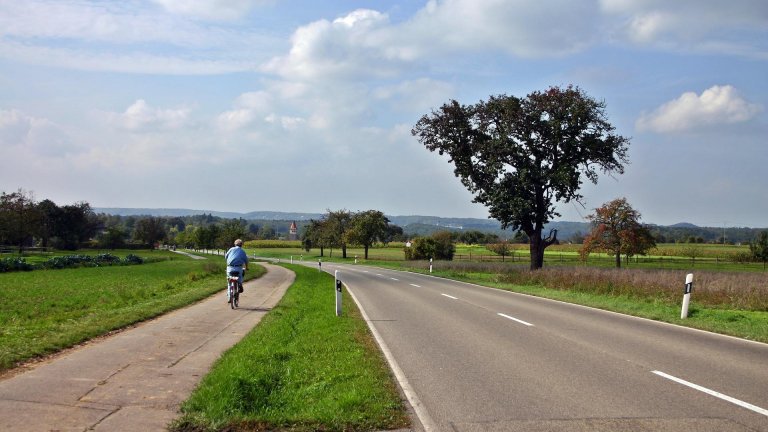 Eine Landstraße mit separatem Radweg auf dem ein Radfahrer fährt.