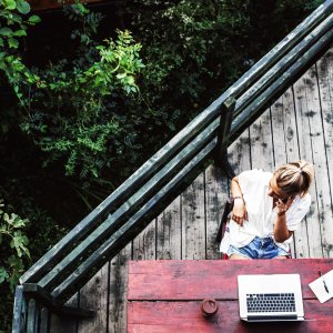 Blick von oben auf Frau mit Laptop, die auf der Terrasse sitzt